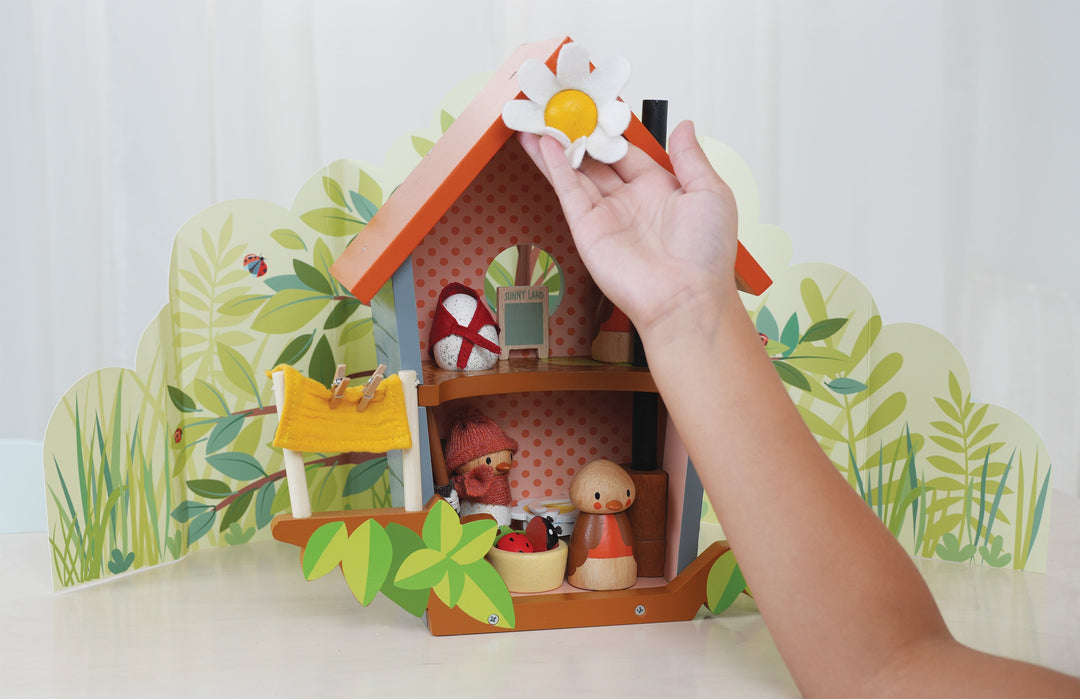 Hand holding a small wooden house with decorative items against a white background