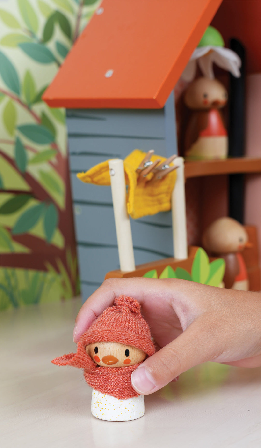Small figurine of a character wearing a red hat and scarf, held by a hand with a colourful background.