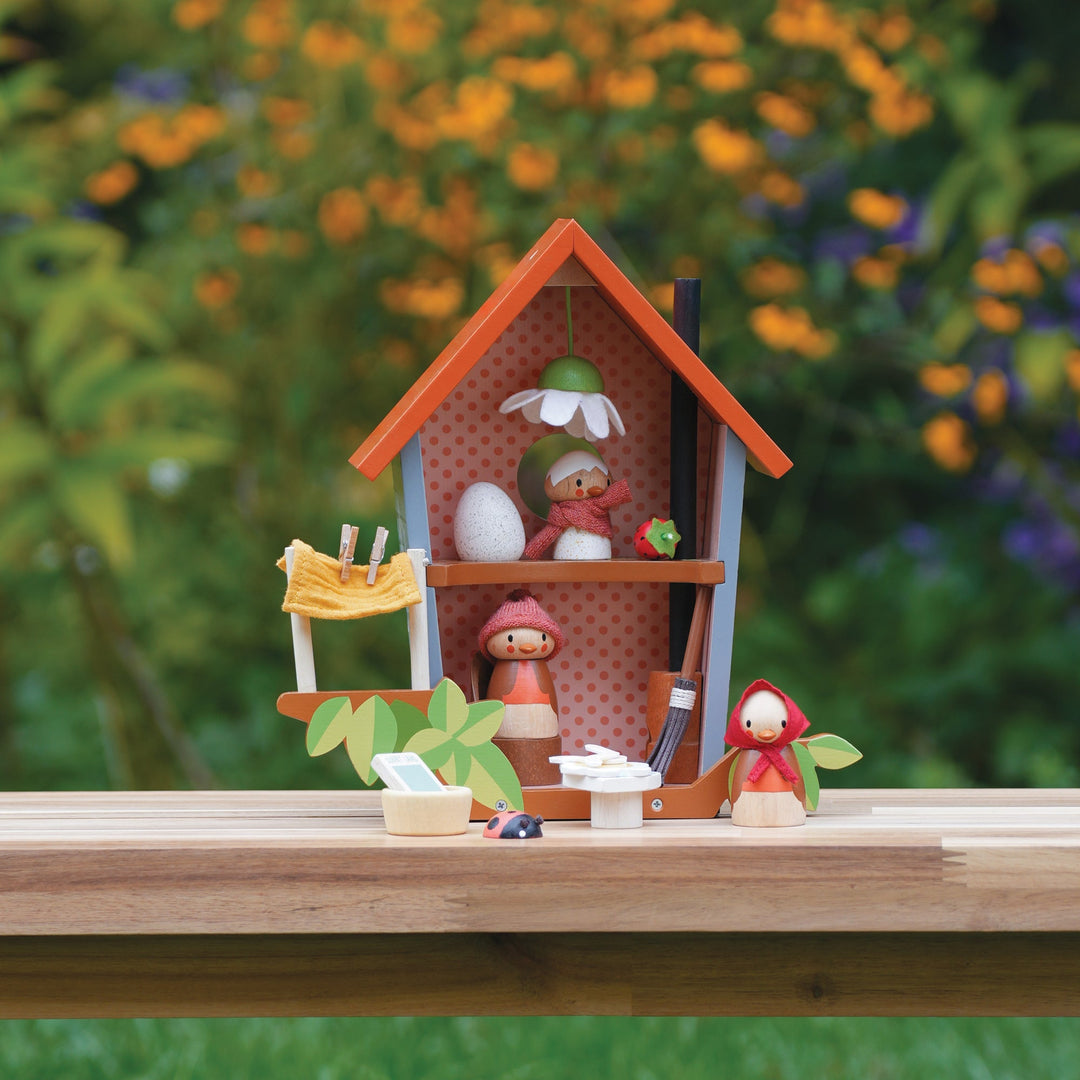 Toy house with small figures on a wooden surface with a blurred natural background