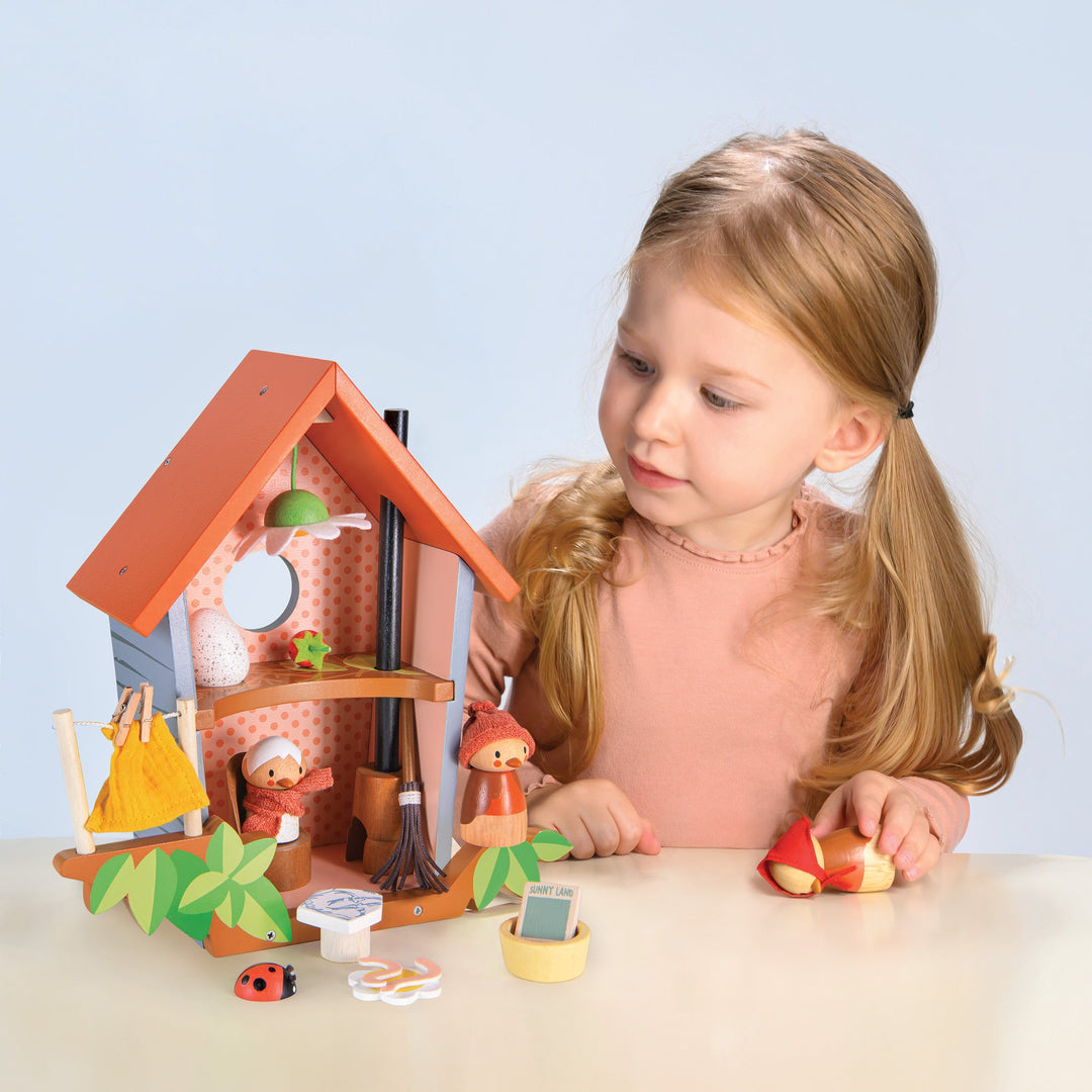 Young girl playing with a wooden bird house and accessories on a light blue background