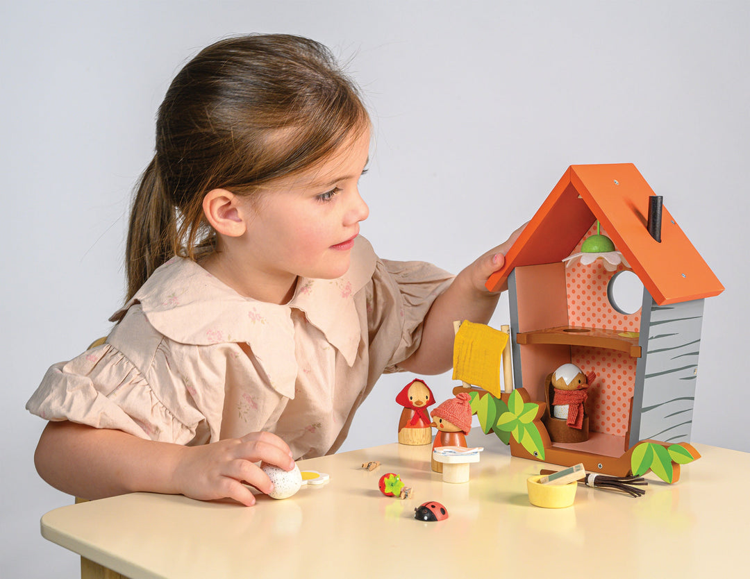 Child playing with a toy bird house and figures on a table