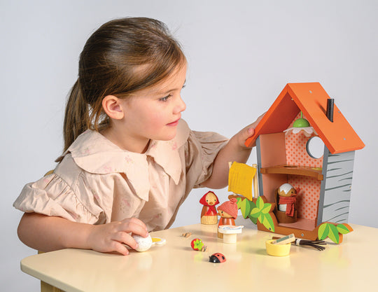 Child playing with a toy bird house and figures on a table