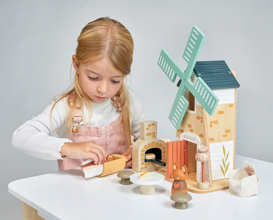 Young girl playing with a wooden toy set on a table against a plain background