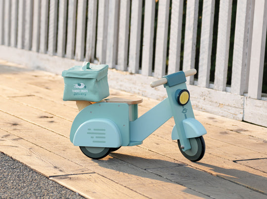 Light blue children's scooter with a basket on a wooden deck.
