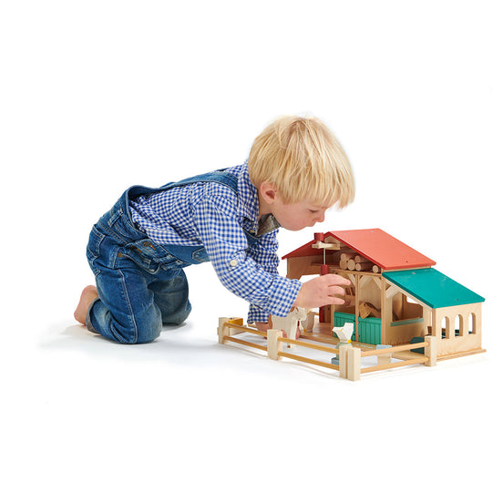 Child playing with a wooden toy barn on a white background