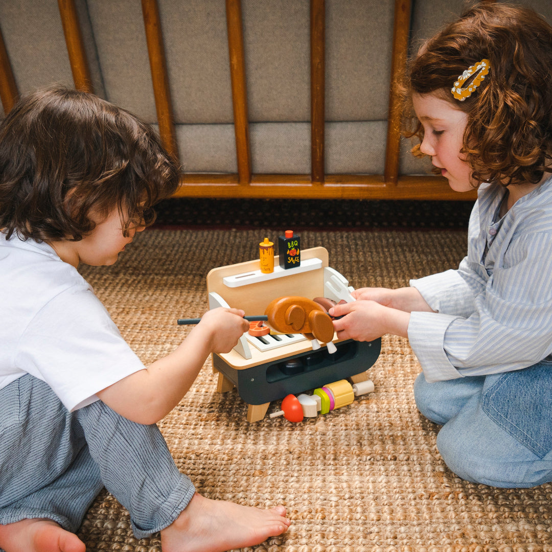 Two children playing with a toy barbecue on a woven mat.