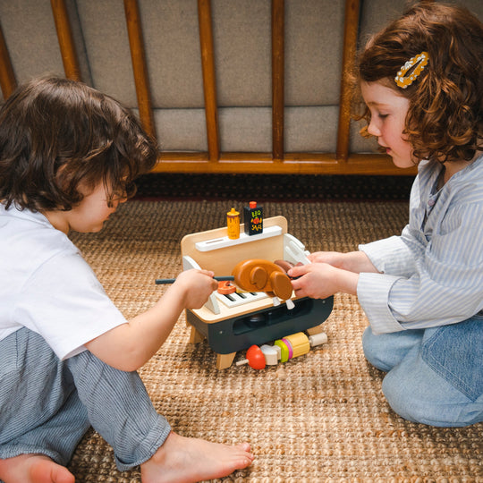 Two children playing with a toy barbecue on a woven mat.
