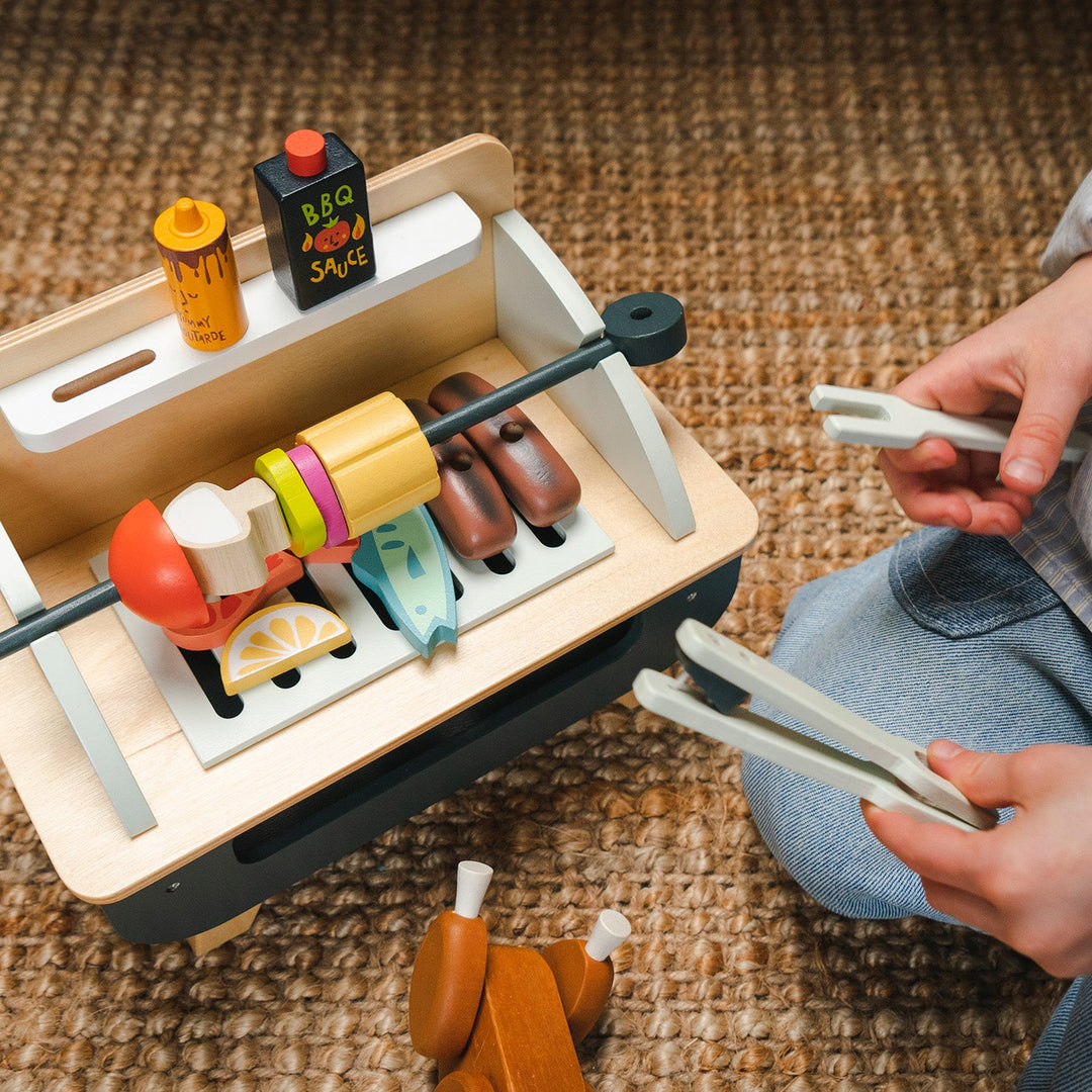Toy barbecue set with skewers and grill on a textured surface