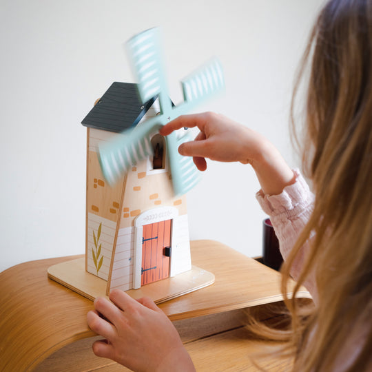Child playing with a toy windmill and house set on a wooden surface.