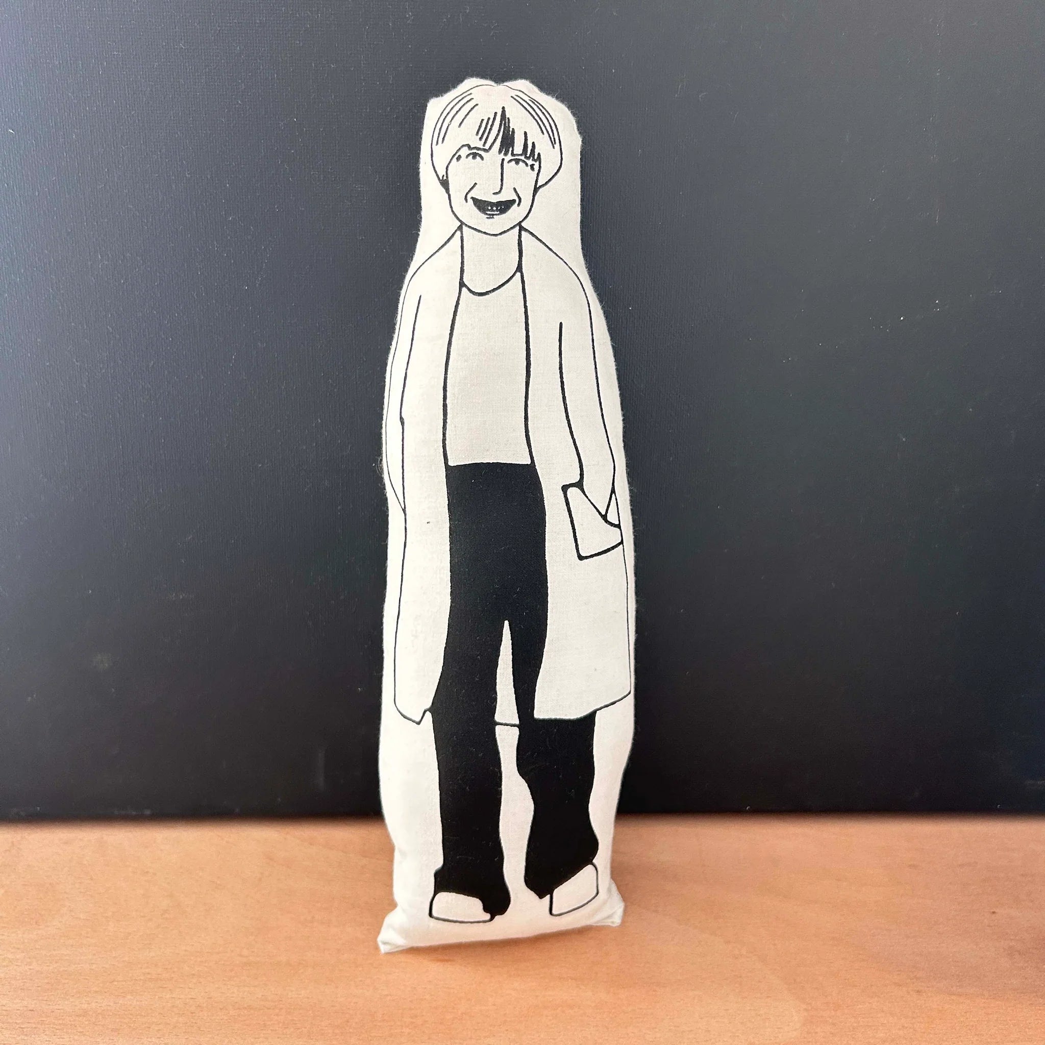 Black and white screen printed doll depicting Victoria Wood on a wooden surface with a dark background