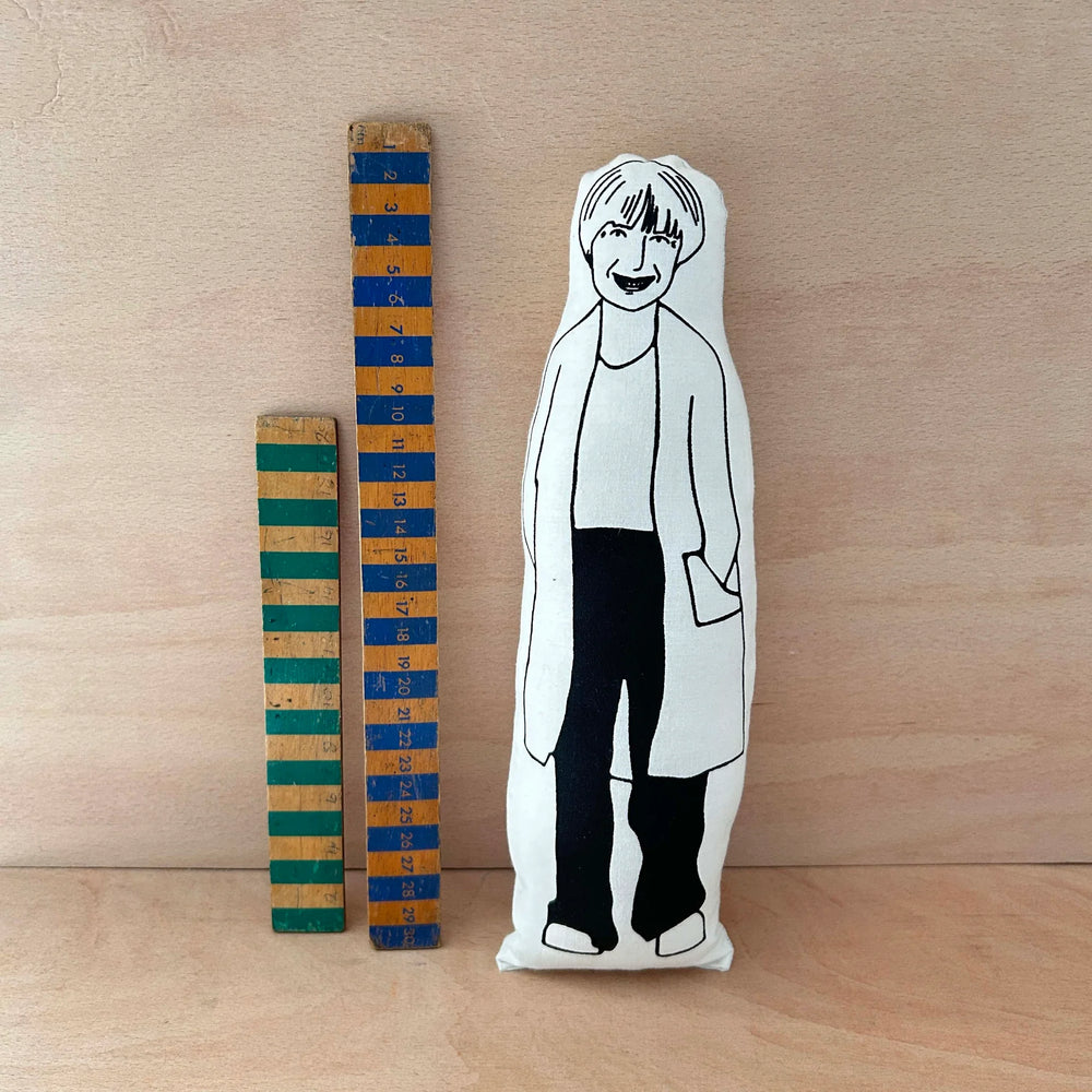Plush toy of a screen printed Victoria Wood doll with a wooden ruler on a wooden surface