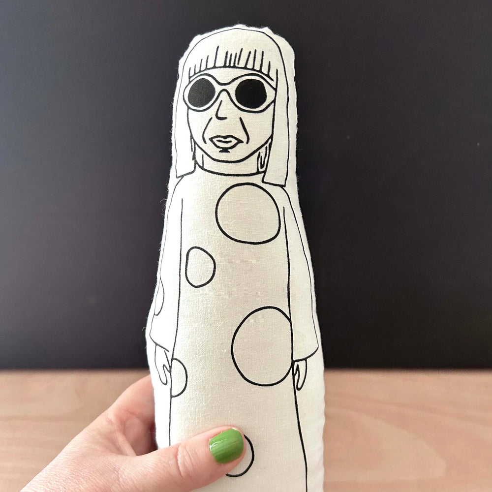 Hand holding a screen printed doll with black and white design against a dark background