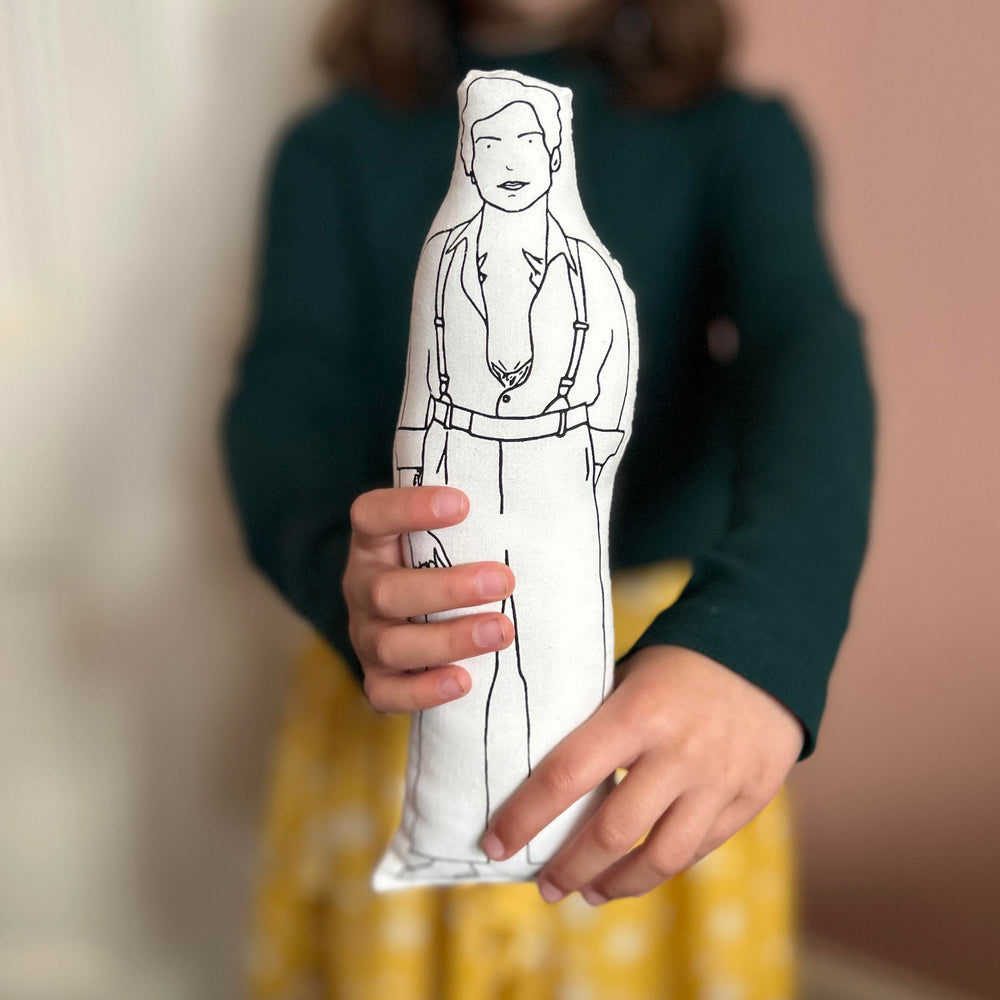 A child holding out a screen printed doll cushion of Harry Styles towards the camera with a blurred background