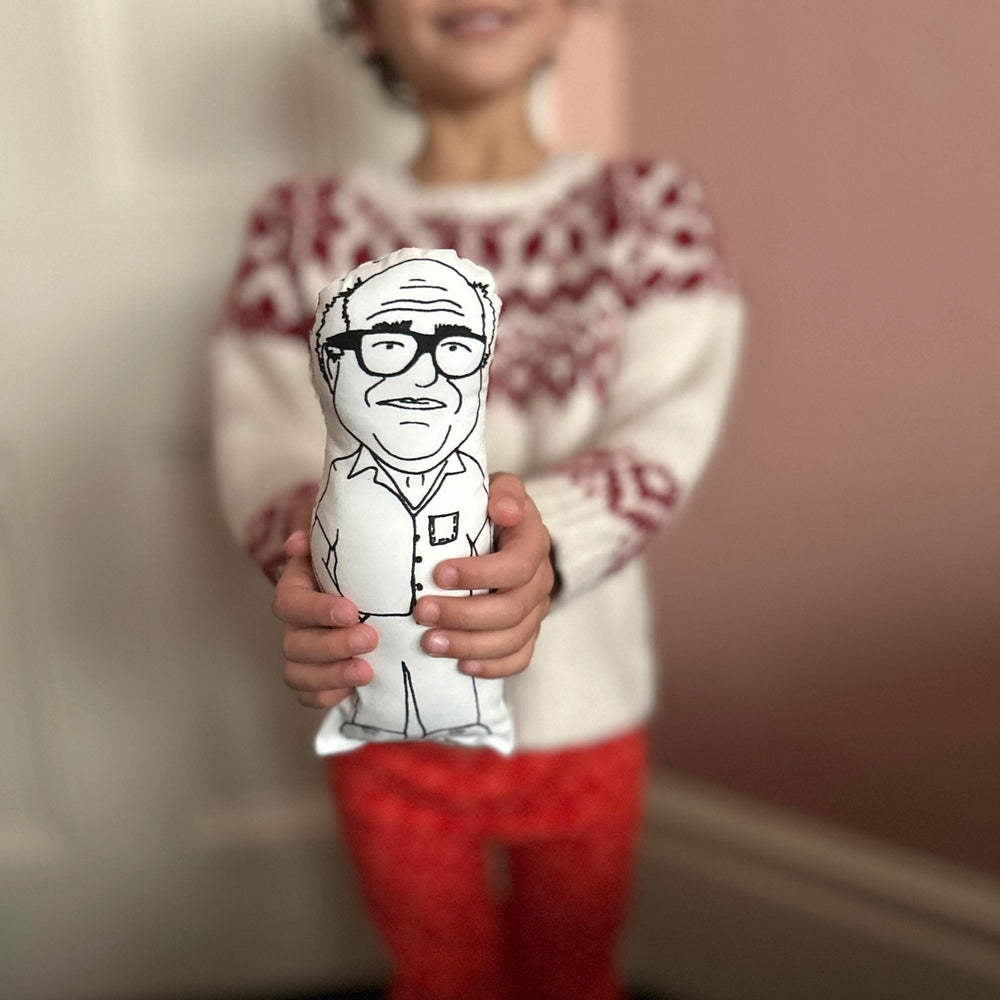 A child holding a black and white cushion doll with a screen printed design of Danny DeVito