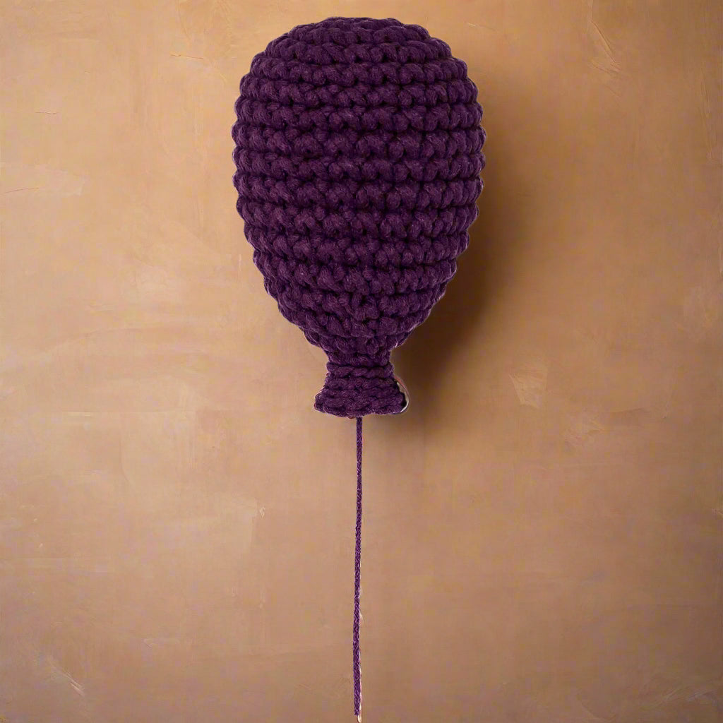 Handmade crochet balloon in aubergine colour, hanging as a wall decoration.