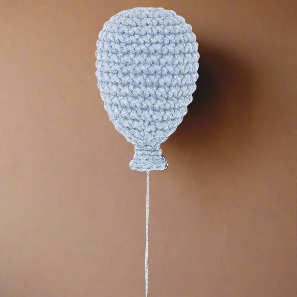 A baby blue handmade crochet balloon with a string attachment, displayed against a wall background.