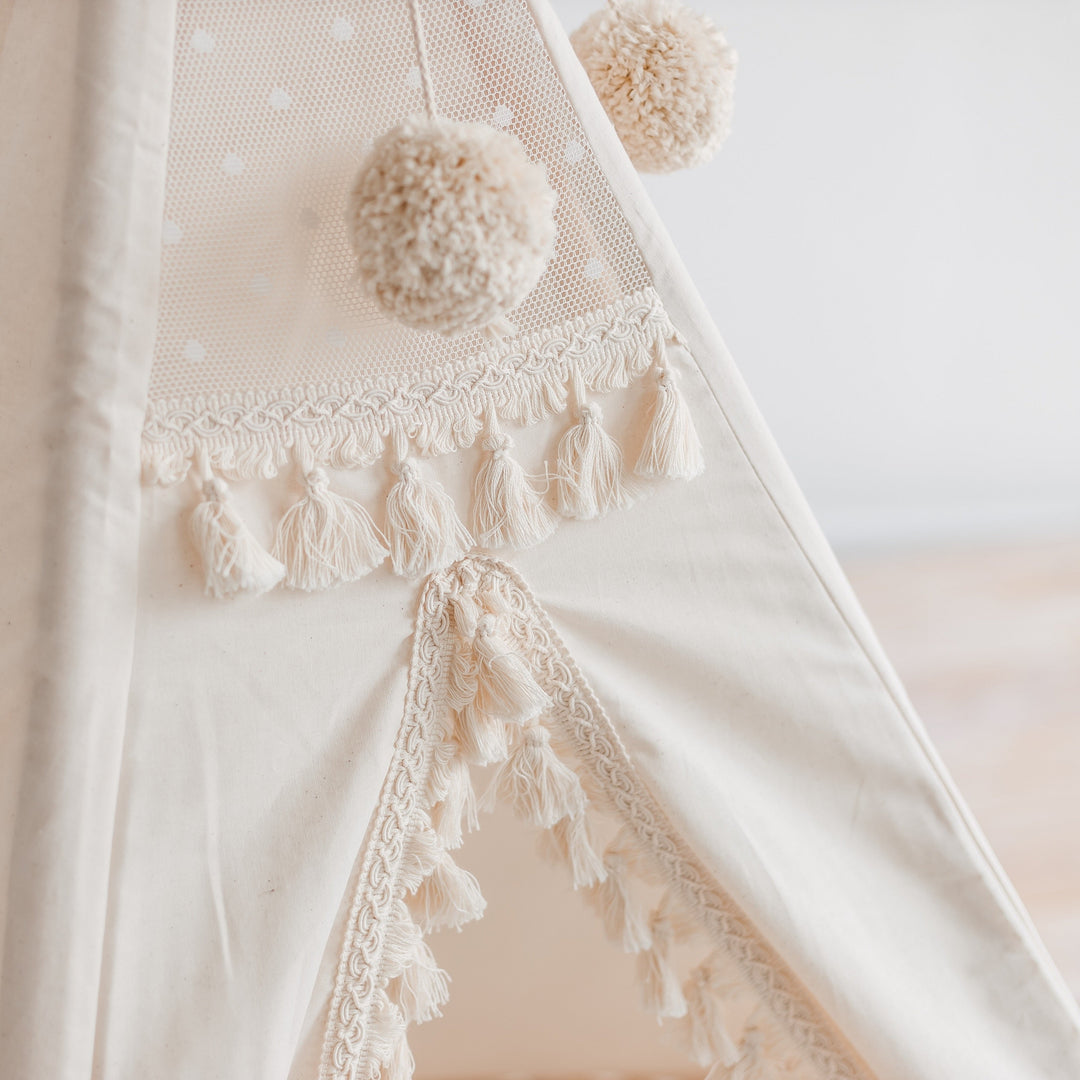 Close up of decorative details on the teepee, such as an intricate lace detail, tassles and round pom poms