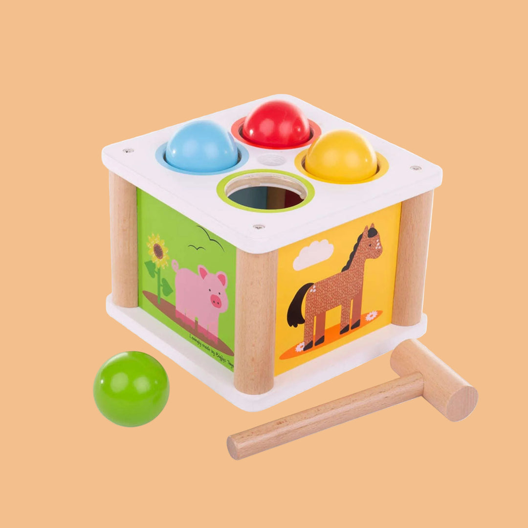 Wooden shape sorting cube with colorful balls and a hammer on a white background