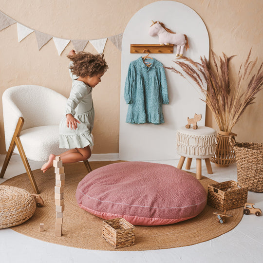 Child playing in a playroom with a pink cushion, wooden blocks, and a white chair.