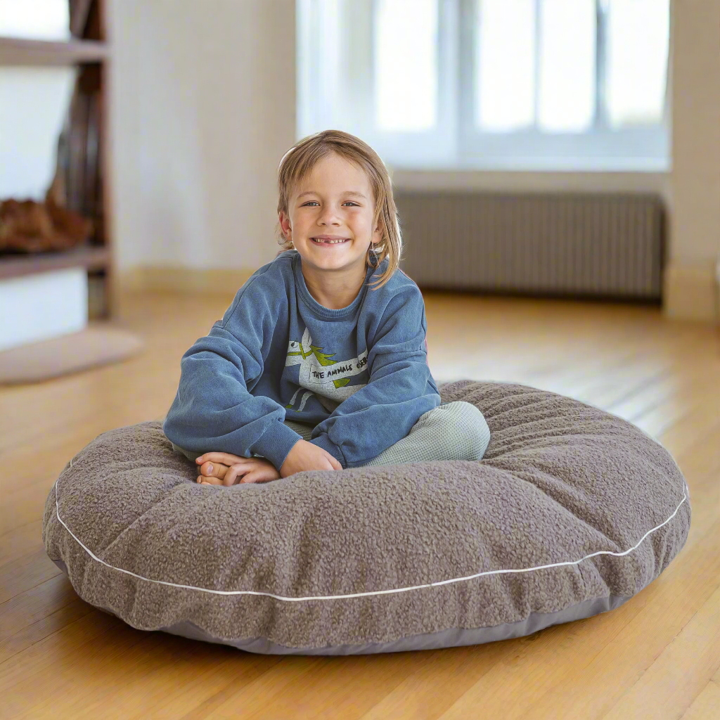 Child sitting on a large round grey floor cushion