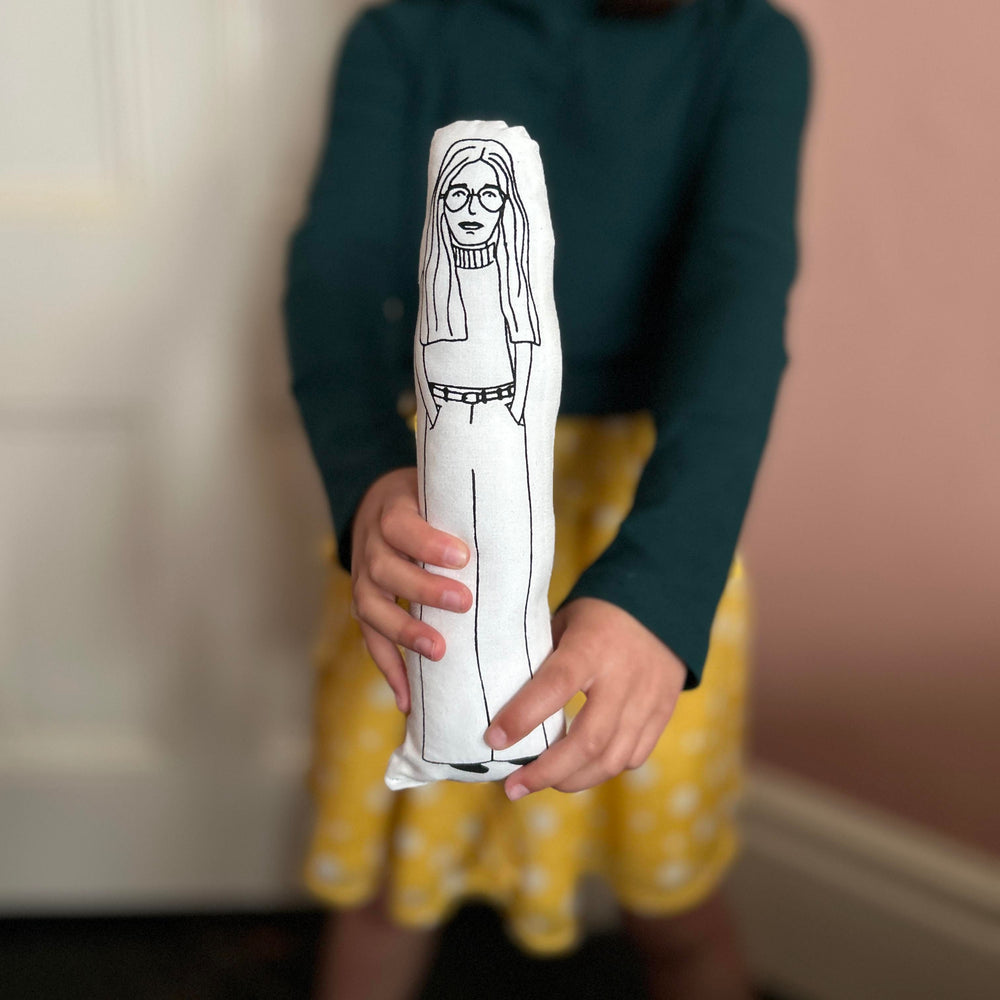 A child holding out screen printed doll cushion of Gloria Steinem towards the camera