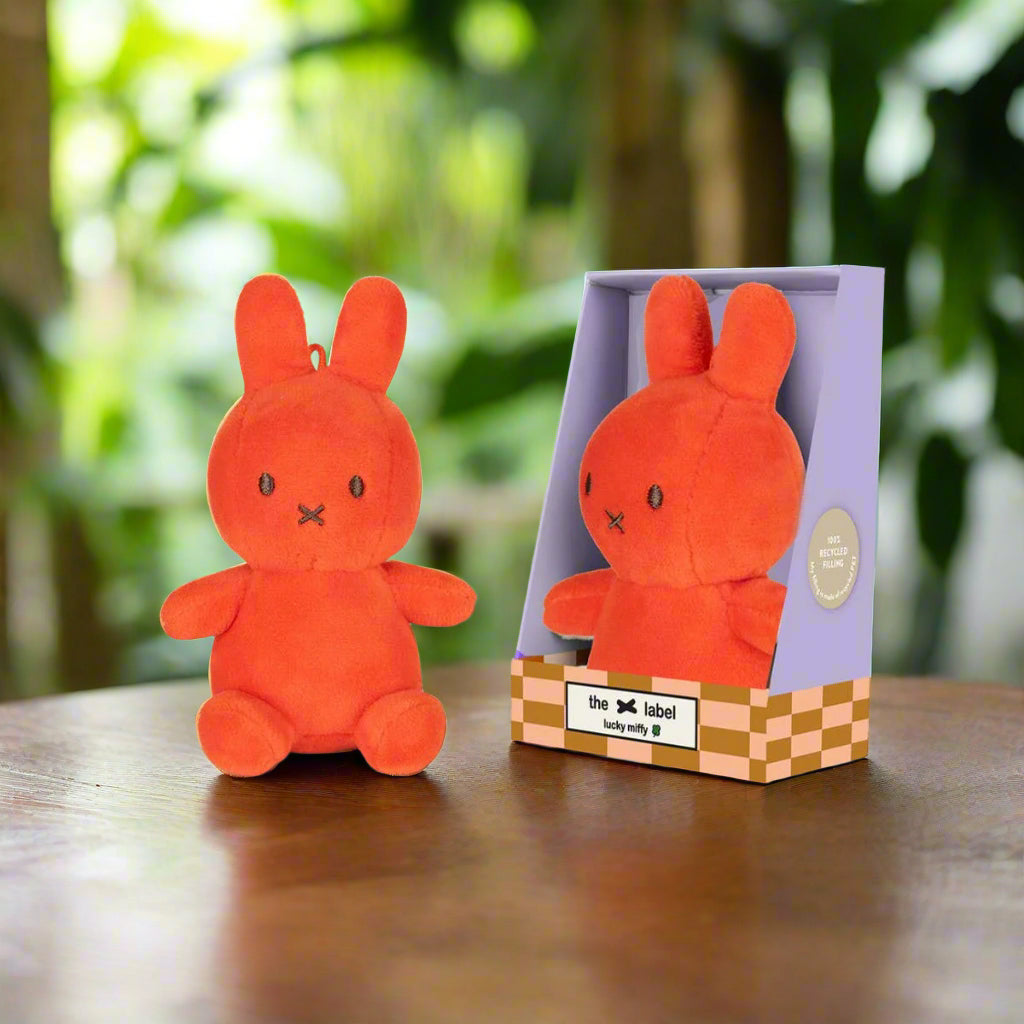 Bright coral orange stuffed toy rabbit with iconic cross stitched mouth in purple gift box
