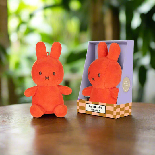 Bright coral orange stuffed toy rabbit with iconic cross stitched mouth in purple gift box