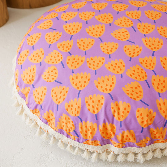 Close up of round floor cushion showing more detail of the orange tulip design with the purple background and the white tassel trim