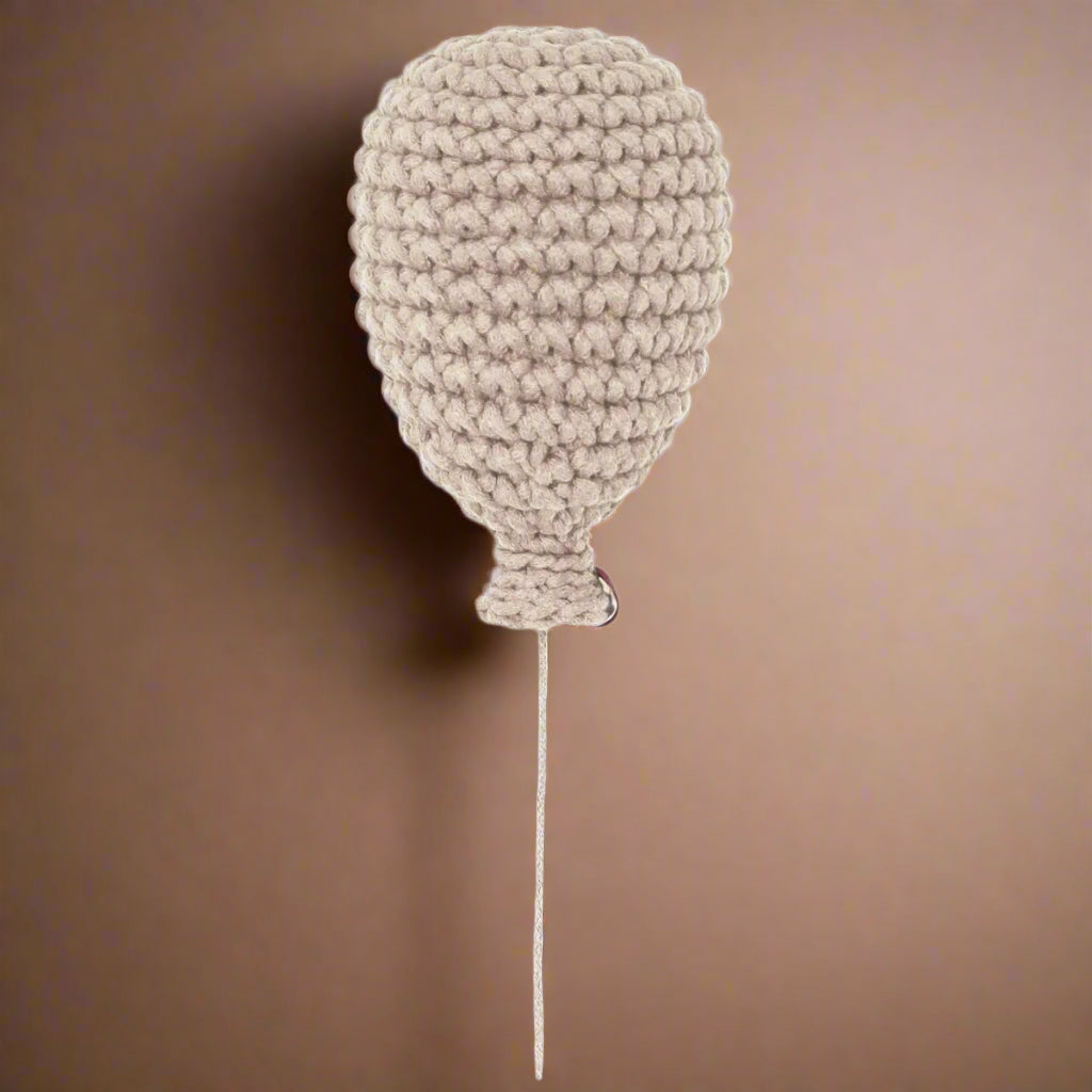 A handmade crochet balloon in beige, with a string attachment at the bottom.