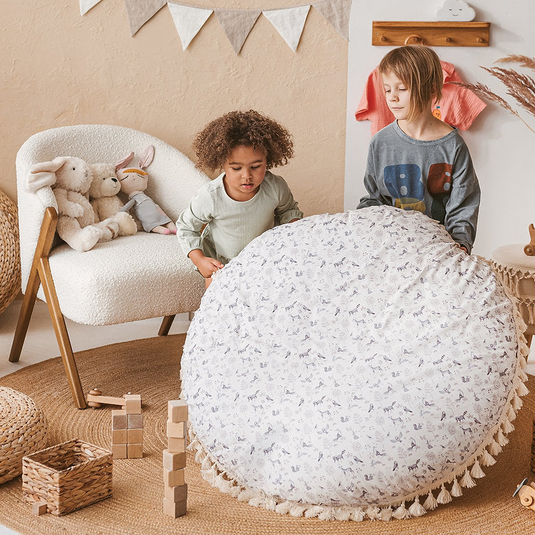 Two children playing with a large white textured ball in a room with a chair and toys.