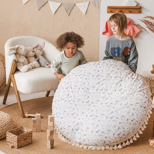 Two children playing with a large white textured ball in a room with a chair and toys.