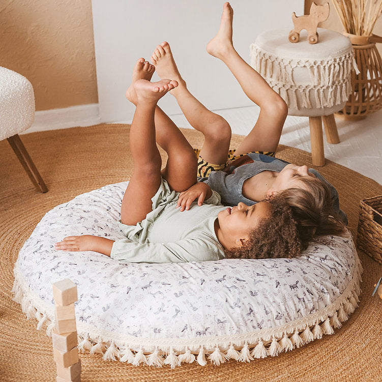 Two children lying on a round cushion in a cosy room with wooden furniture.