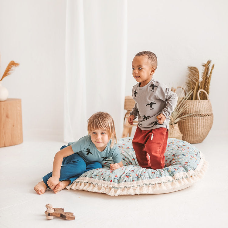 Two children playing on a round cushion in a bright room with white walls and wooden furniture.