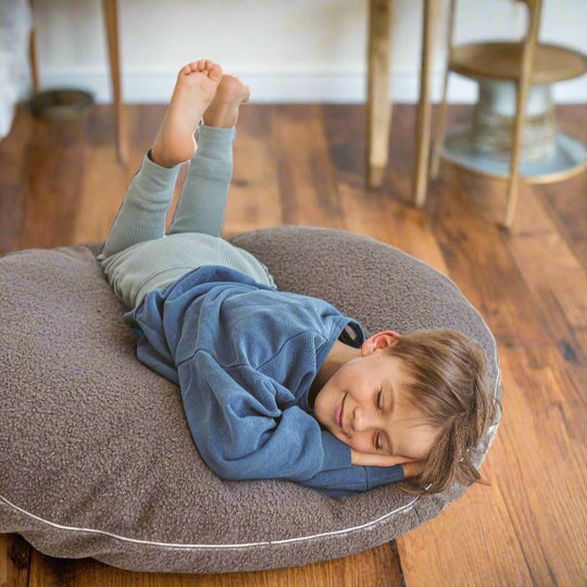 Child lying on large round grey floor cushion