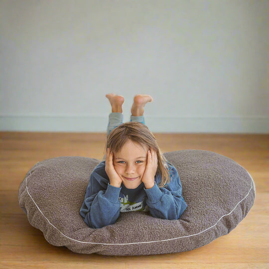 Child lying on grey floor cushion with his face in his hands and his feet in the air