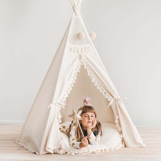 Child playing inside a white teepee with a plain background