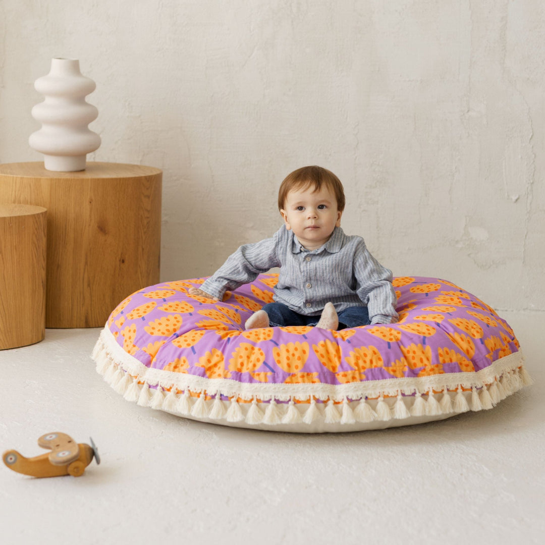 Child sitting on a colourful circular cushion with wooden furniture and a plain wall in the background