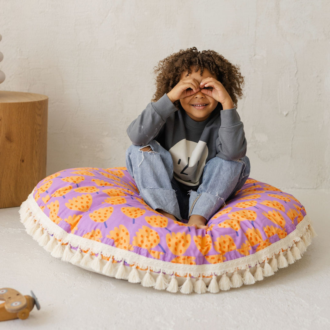 Child sitting on a colourful round cushion holding their hands up to their eyes like binoculars