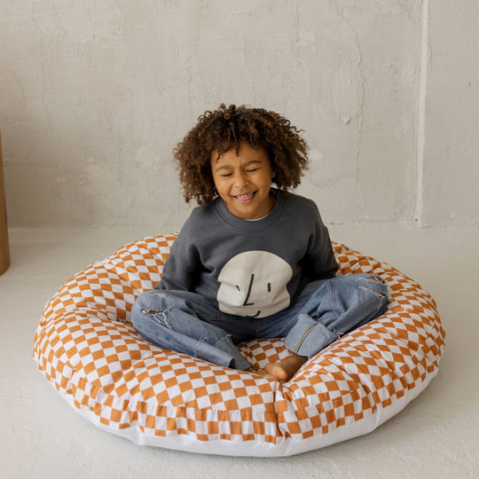Child sitting on a chequered cushion with a plain background