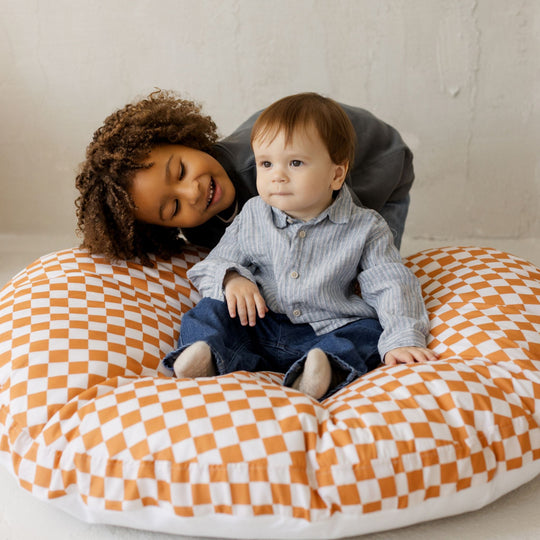 Two children sitting on a large orange and white chequered floor cushion