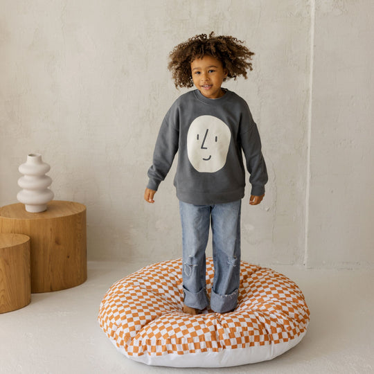 Child standing on orange abd white chequered floor cushion