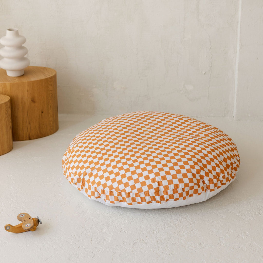 Round chequered pillow on a light surface with wooden objects in the background