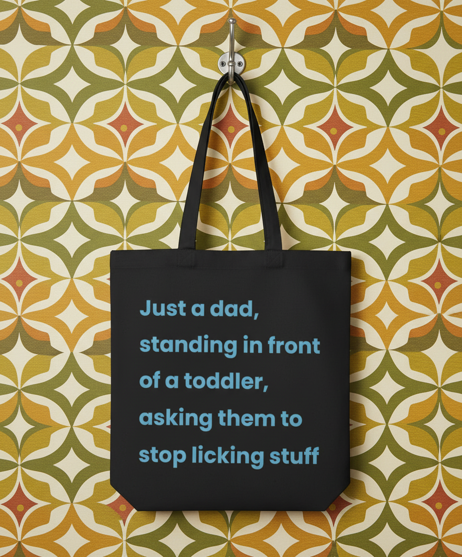 Black tote bag with humorous text on a patterned wall background