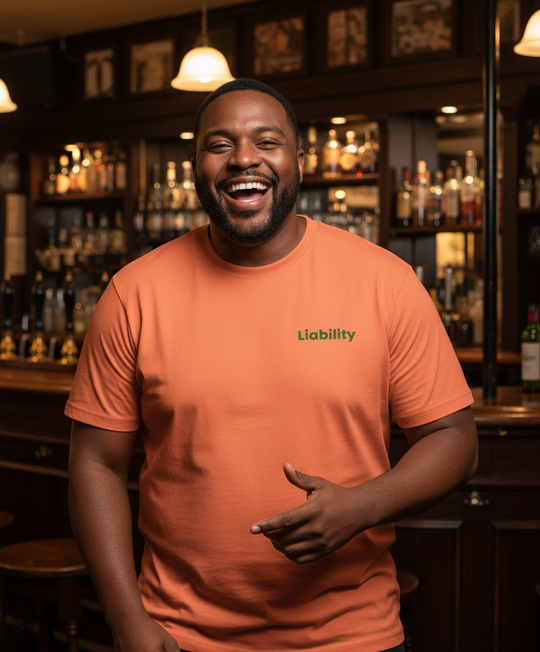 Man wearing an orange t-shirt with 'Liability' printed on it, standing in a bar.