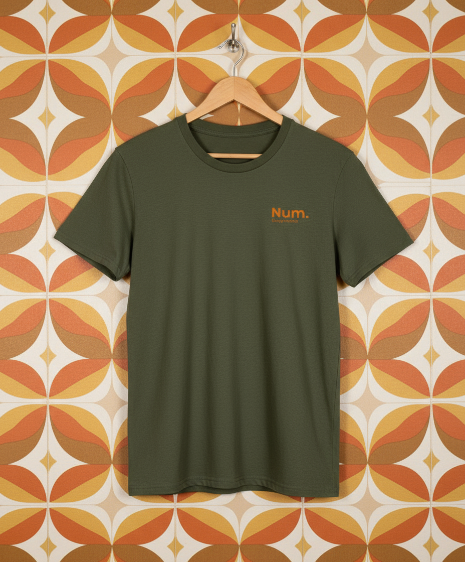 Green t-shirt with 'Num' logo on a hanger against a patterned wall.