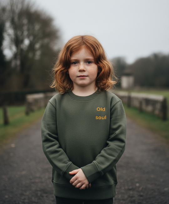 Child wearing a green sweatshirt with 'Old soul' text, standing on a path with a blurred background