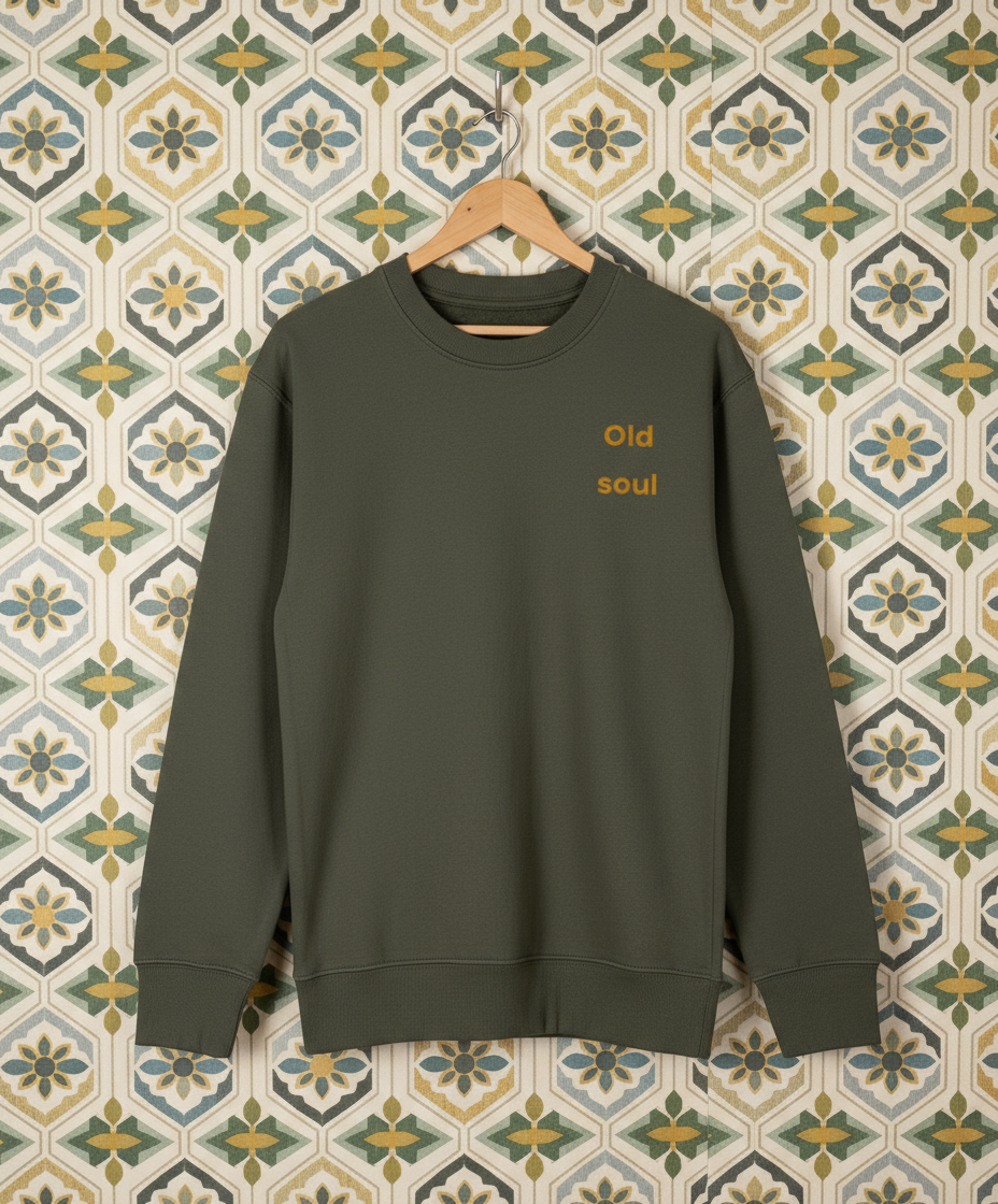 Green sweatshirt with 'Old soul' text on a hanger against a patterned wall.