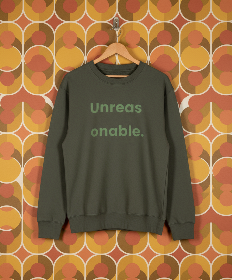 Green sweatshirt with 'Unreasonable' text on a hanger against a patterned wall.