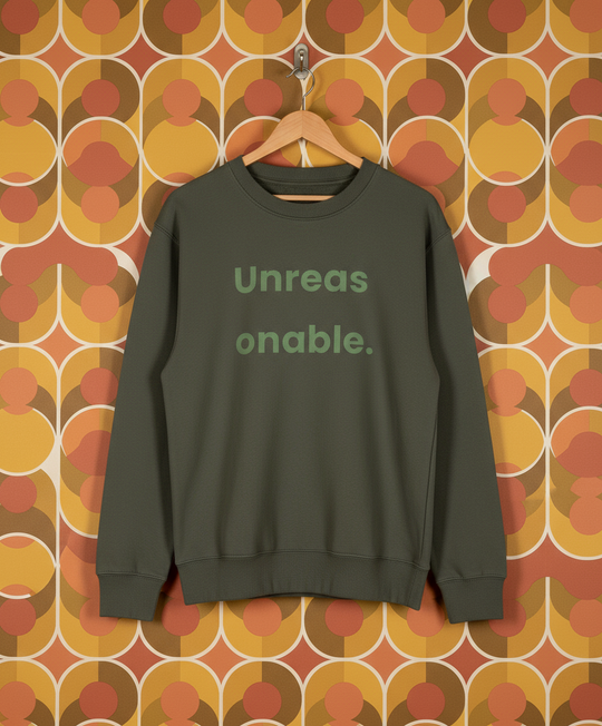 Green sweatshirt with 'Unreasonable' text on a hanger against a patterned wall.