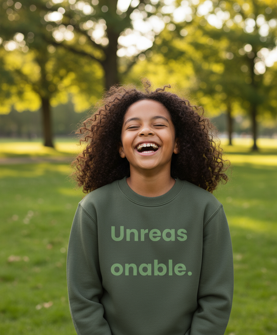 Child wearing a green sweatshirt with text, standing in a park.